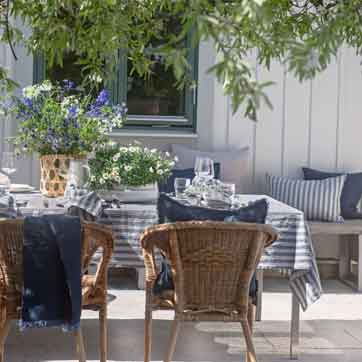 Gedeckter Sommertisch mit Himla Leinentischdecke in Blau-Weiß-Streifen, Servietten und Weidenkorbstühlen